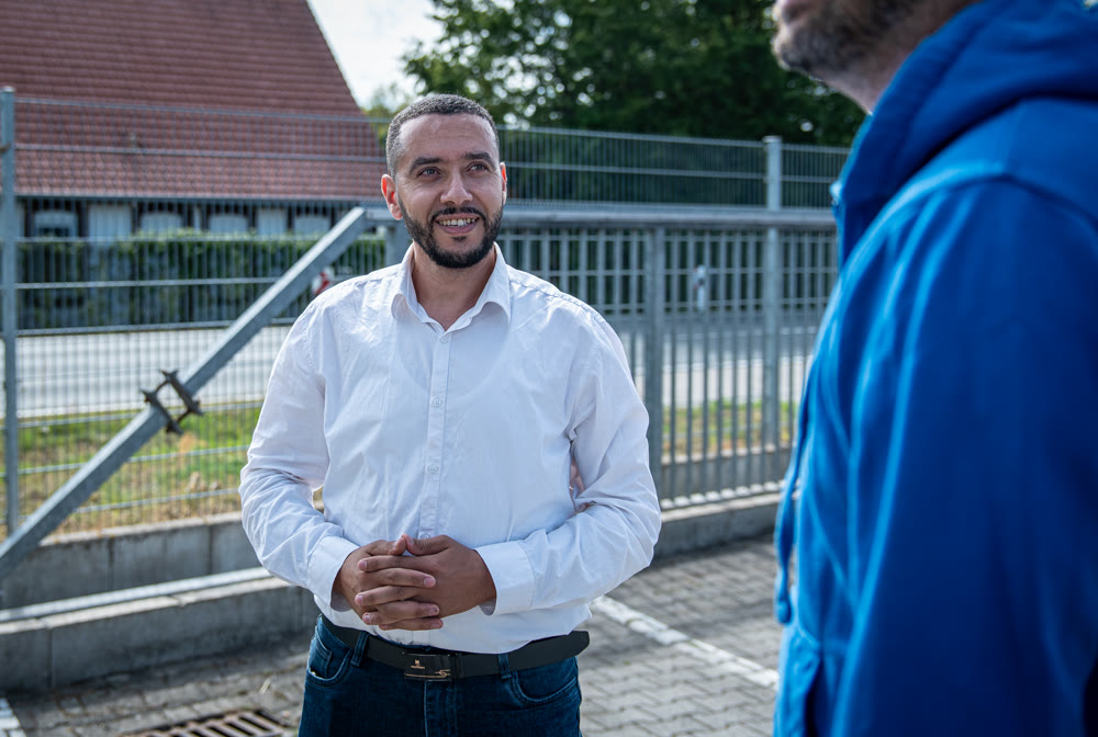 Lockeres Gespräch auf dem Hof: ein angekommener Fahrer lacht im Austausch mit dem DIALOG-Team