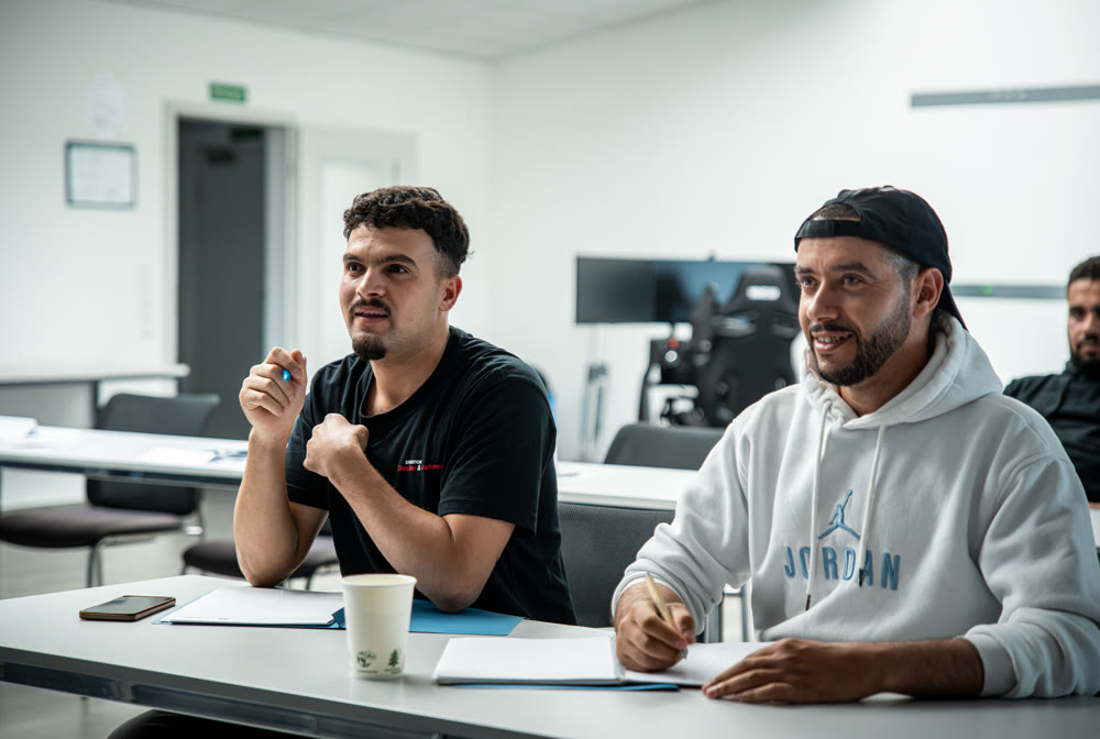 Unterricht bei DIALOG: zwei Teilnehmer folgen aufmerksam dem Kurs, einer macht sich Notizen